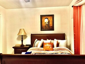 Ein ordentlich bezogenes Bett mit einem Kopfkissen, auf dem ‘worth it’ steht, in einem Hotelzimmer mit einem gerahmten Bild an der Wand und einer Lampe auf dem Nachttisch.