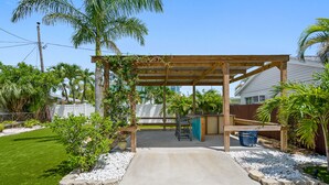A covered patio area with a concrete floor, surrounded by a brick border, and a wooden pergola structure.