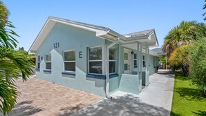 A light blue house with the number 131 and the letter E on the side, a paved driveway, and surrounding greenery.