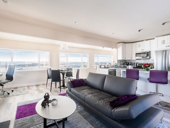A modern apartment with a living area, kitchen, and large windows offering a city view.