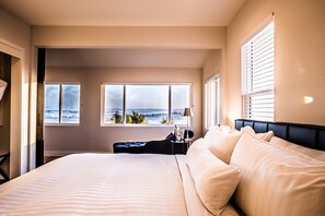 A hotel room with a large bed, a view of the city, and a window with blinds.