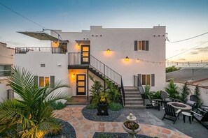 Una casa moderna de dos pisos con un patio, mobiliario exterior y una escalera que lleva al nivel superior.