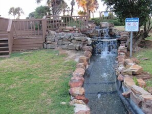 Une petite cascade décorative, agrémentée d’un panneau d’avertissement, entourée d’une bordure en pierre et d’une clôture en bois.