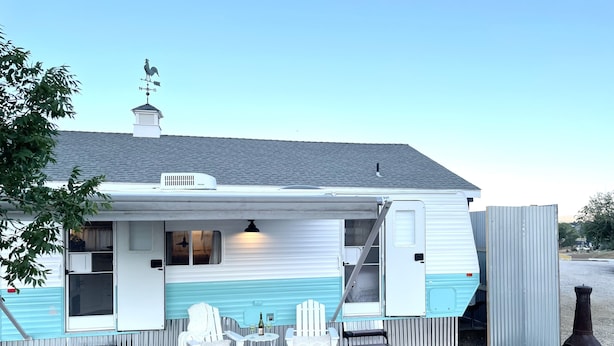 A mobile home with a deck, white furniture, and a barbecue grill.