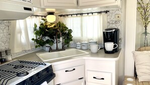 A compact kitchen with a gas stove, white cabinets, a coffee maker, and a potted plant.