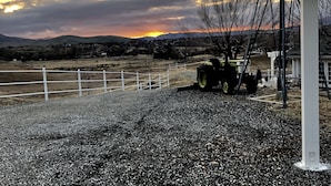 A rural landscape with a windmill, a tractor, and a fenced area.
