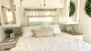 A bedroom with a bed, a bedside table with a clock, a potted plant, and a mirror.