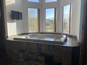 Un baño con una bañera grande, tres ventanas y un televisor de pantalla plana.
