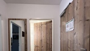 Un couloir avec une porte en bois, un miroir et un sol carrelé.