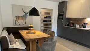 Une cuisine moderne avec des meubles gris, une table à manger en bois et un luminaire suspendu noir.
