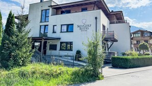 Il s’agit d’un bâtiment moderne sur lequel on peut lire l’inscription « Ski & Golf Suites ». Sa façade est un mélange de verre et de bois, elle est dotée de nombreuses fenêtres et d’un escalier menant à un étage supérieur.