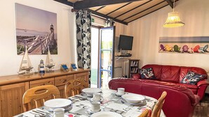 Uma sala de jantar com uma mesa posta para quatro pessoas, um sofá vermelho, uma televisão e um quadro de uma ponte.