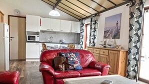 Uma sala de estar moderna com um sofá de couro vermelho, uma mesa de centro de madeira e uma cozinha ao fundo.