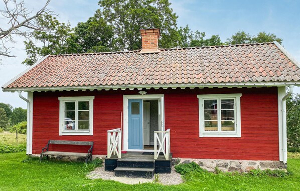 Une maison en bois rouge avec un toit en tuiles, une porte bleue et un banc à l’extérieur.