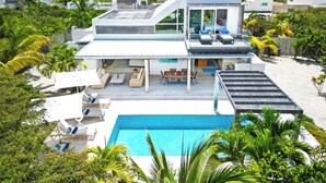 Una casa moderna con piscina, mobiliario exterior y un porche cubierto.