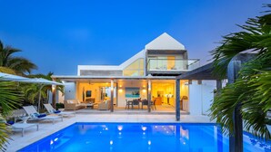 Una casa moderna con piscina, mobiliario exterior y un interior bien iluminado.