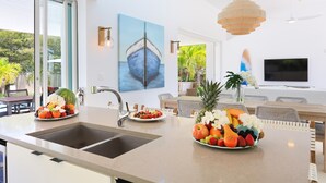 Una cocina moderna con una isla grande, un comedor con mobiliario de mimbre y un televisor montado en la pared.