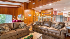 A spacious living room with leather sofas, a wooden staircase, and a view of the outdoors. - Mountain Dreams- Peaceful, Charming, Pet Friendly (Maggie Valley)