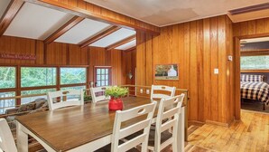 A wooden-paneled room with a dining table and chairs, a red vase with flowers, and a bed with a checkered blanket. - Mountain Dreams- Peaceful, Charming, Pet Friendly (Maggie Valley)