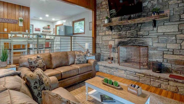 A cozy living room with a stone fireplace, a leather sofa, and a television mounted on the wall. - Mountain Dreams- Peaceful, Charming, Pet Friendly (Maggie Valley)