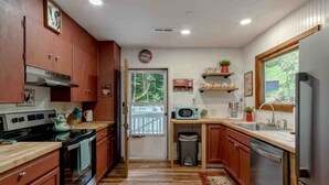 A kitchen with wooden cabinets, a stove, a microwave, and a refrigerator. - Mountain Dreams- Peaceful, Charming, Pet Friendly (Maggie Valley)