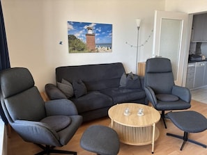 Un salon comprenant un canapé, deux fauteuils, une table basse et un tableau représentant un phare, accroché au mur.