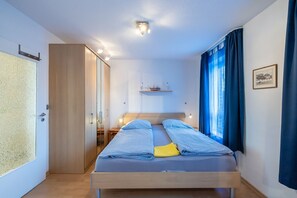 Une chambre avec deux lits, une armoire, un bureau et une petite étagère avec quelques objets.