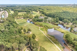 Vista aérea de un campo de golf con varios cuerpos de agua, rodeado de un bosque denso y algunos edificios.