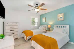 A bedroom with two beds, a ceiling fan, a nightstand with a lamp, and a dresser.