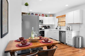 A modern kitchen with white cabinets, a stainless steel refrigerator, and a wooden dining table set with red bowls and wine glasses. - Oktoberfest + Walk to Downtown Helen + Hot Tub (Helen)