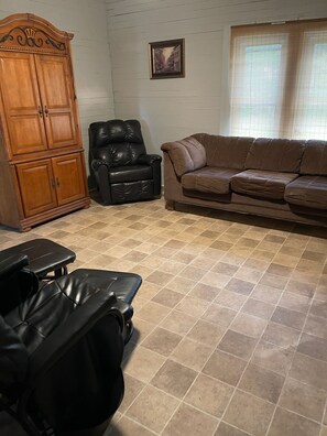 Un salon avec un canapé en cuir marron, un fauteuil en cuir noir, un meuble en bois et une table de massage.