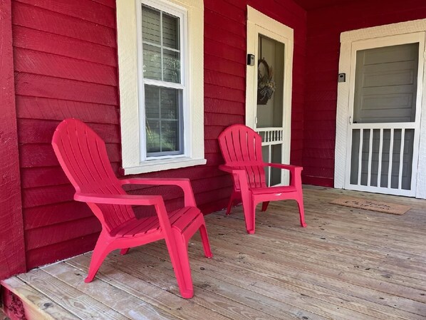 Une maison rouge avec deux chaises Adirondack rouges sur un porche en bois.