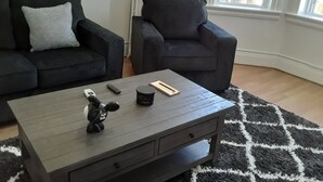 A living room with a dark wooden coffee table, two black armchairs, a grey patterned throw pillow, and a black and white rug.