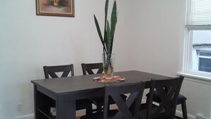 A dining area with a dark wooden table and chairs, a potted plant, and a framed picture on the wall.