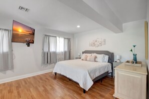 Une chambre à coucher avec un grand lit, une table de chevet, une commode et un téléviseur fixé au mur qui diffuse une scène de coucher de soleil.