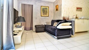 A living room with a dark sofa, a white cabinet, a painting, and a television. - 2 bedroom gorgeous apartment in Orange (Orange)