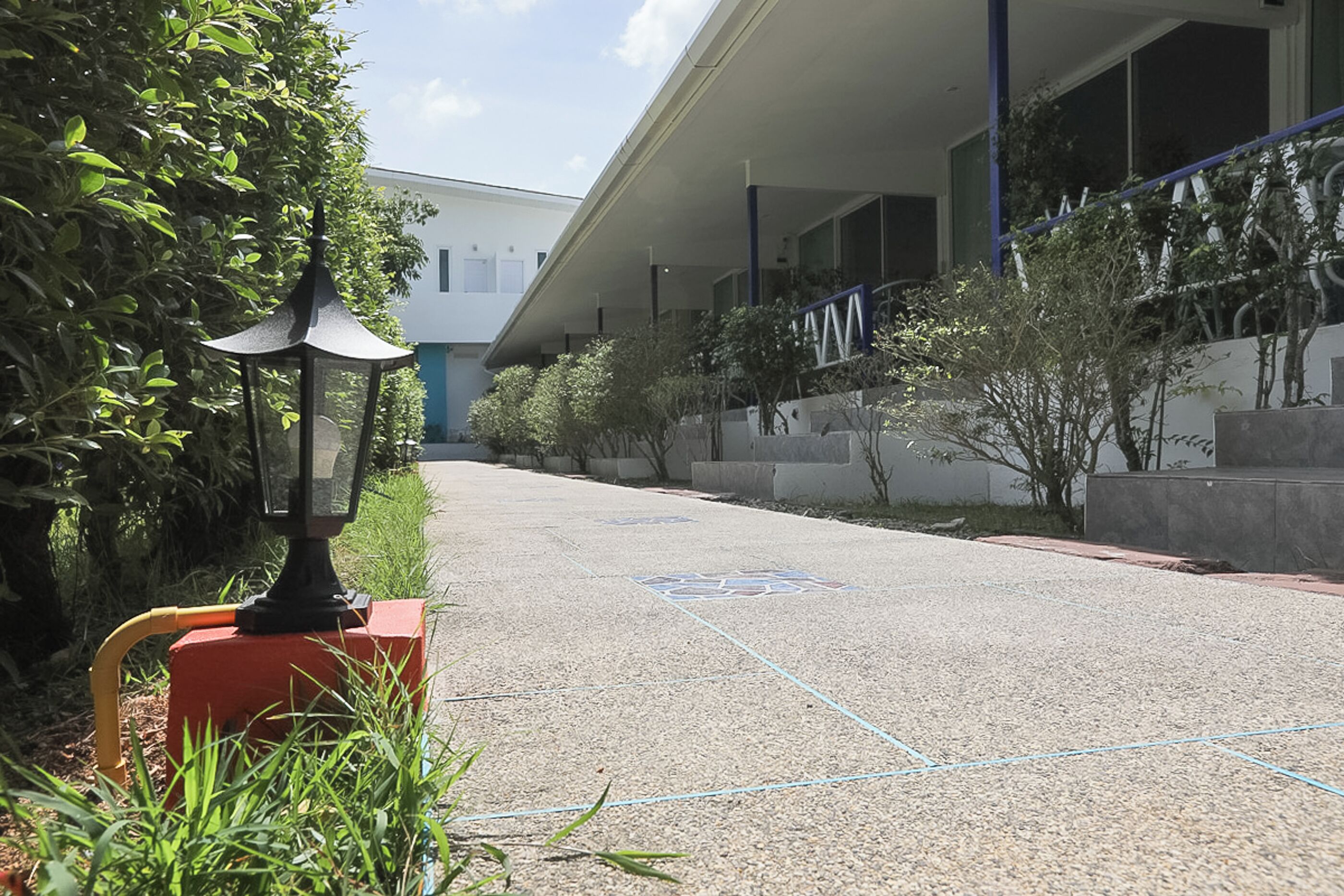 A pathway leading to a building with a blue and white exterior, surrounded by greenery and a red lamp post.