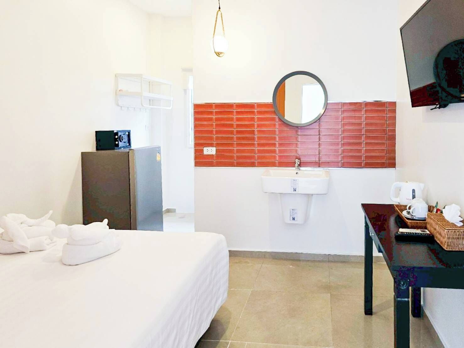 A hotel room with a bed, a sink, a mirror, a television, and a table with a basket.