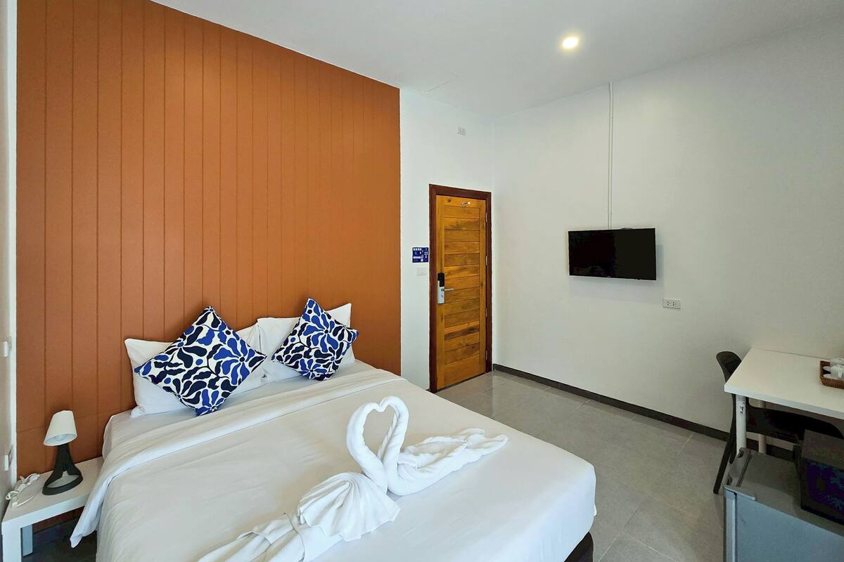 Une chambre d’hôtel avec un lit, un téléviseur fixé au mur, une porte en bois et une petite table sur laquelle se trouve un panier.
