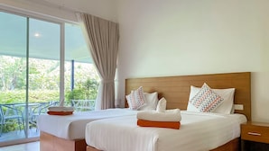 Habitación de hotel con dos camas, cabecero de madera y balcón con vistas a zonas verdes.