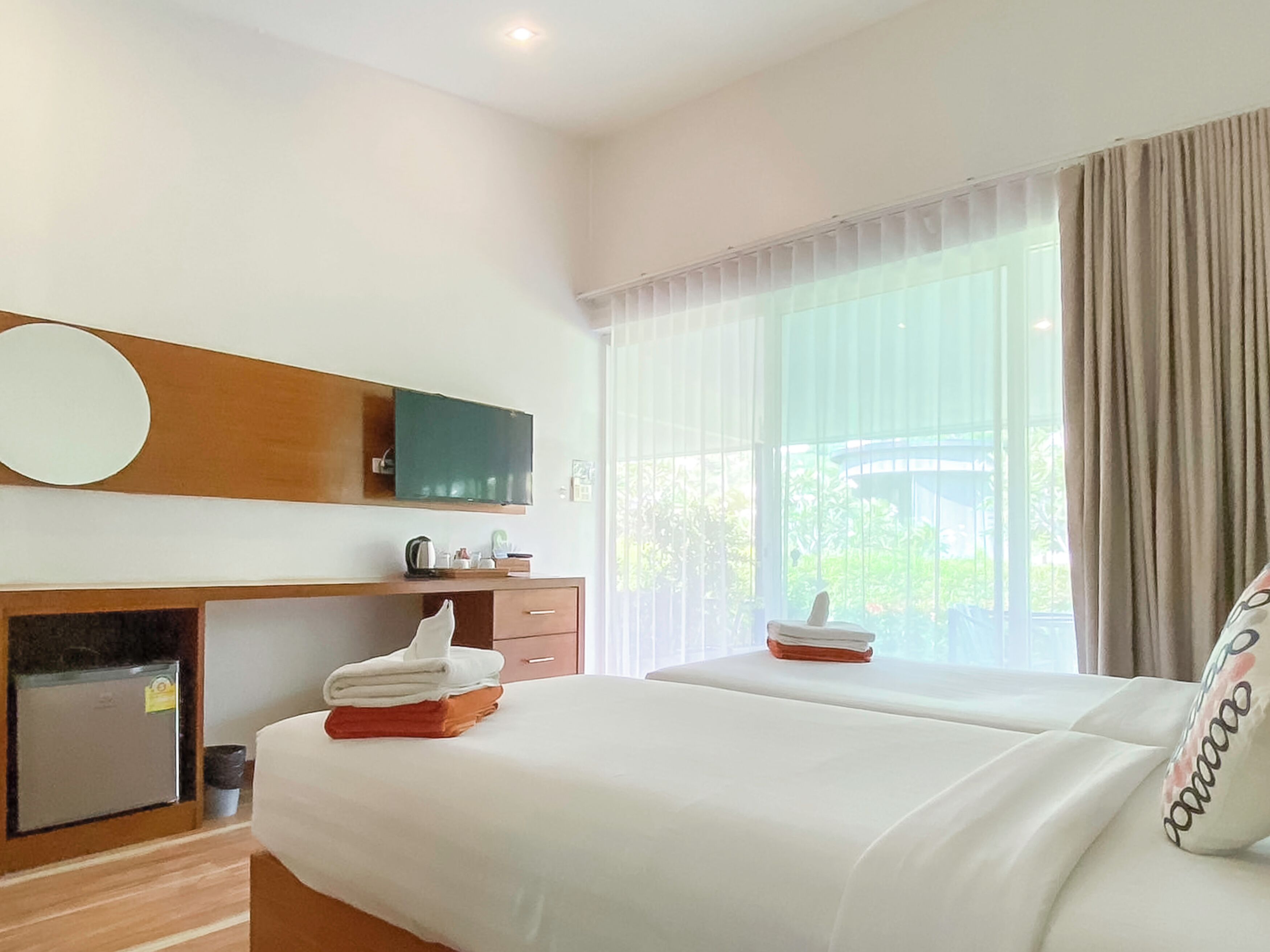Una habitación de hotel con cama, escritorio, televisión y ventana con cortinas.