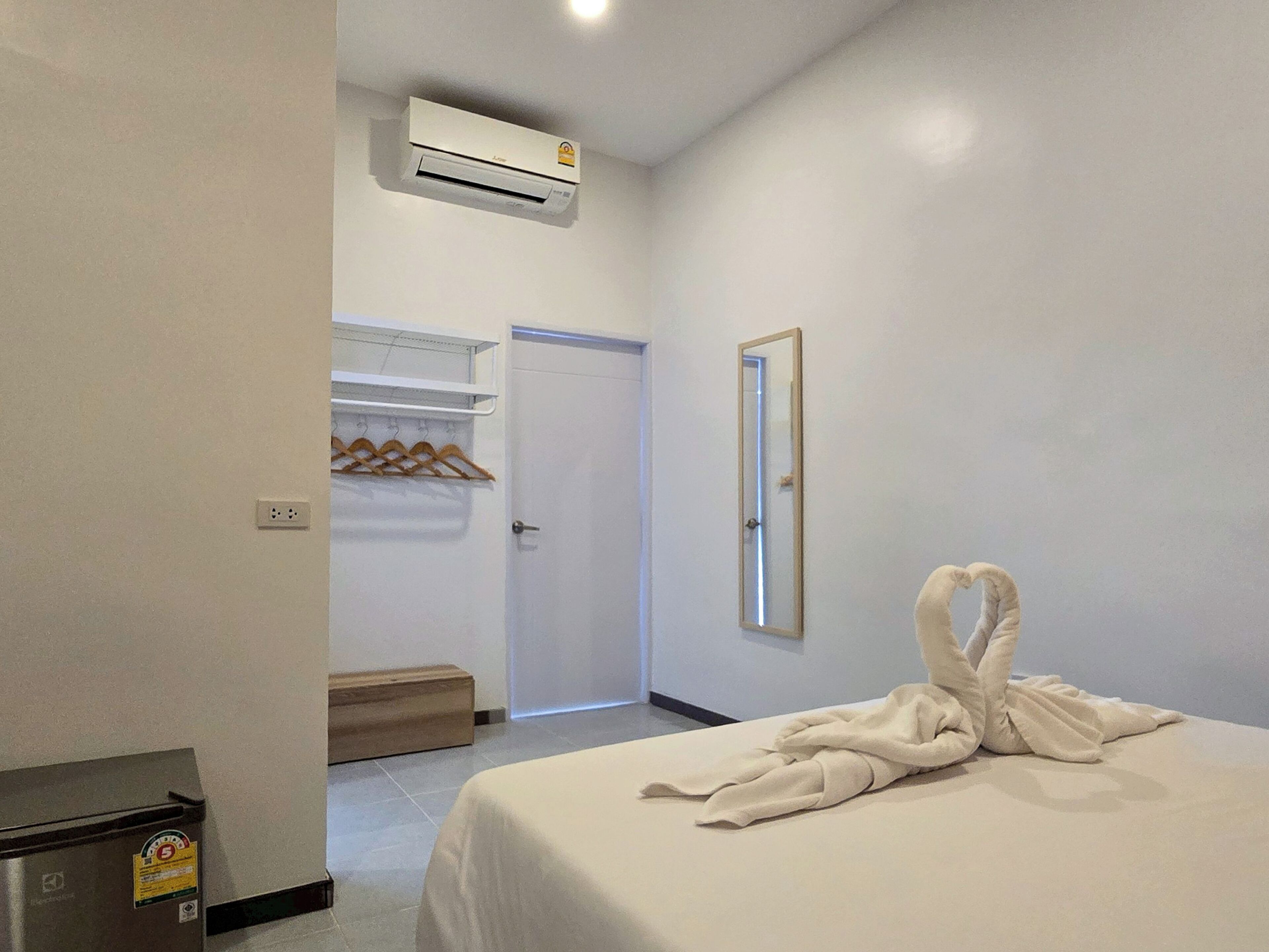 A hotel room with a bed, a mirror, an air conditioning unit, a coat rack, and a wooden bench.
