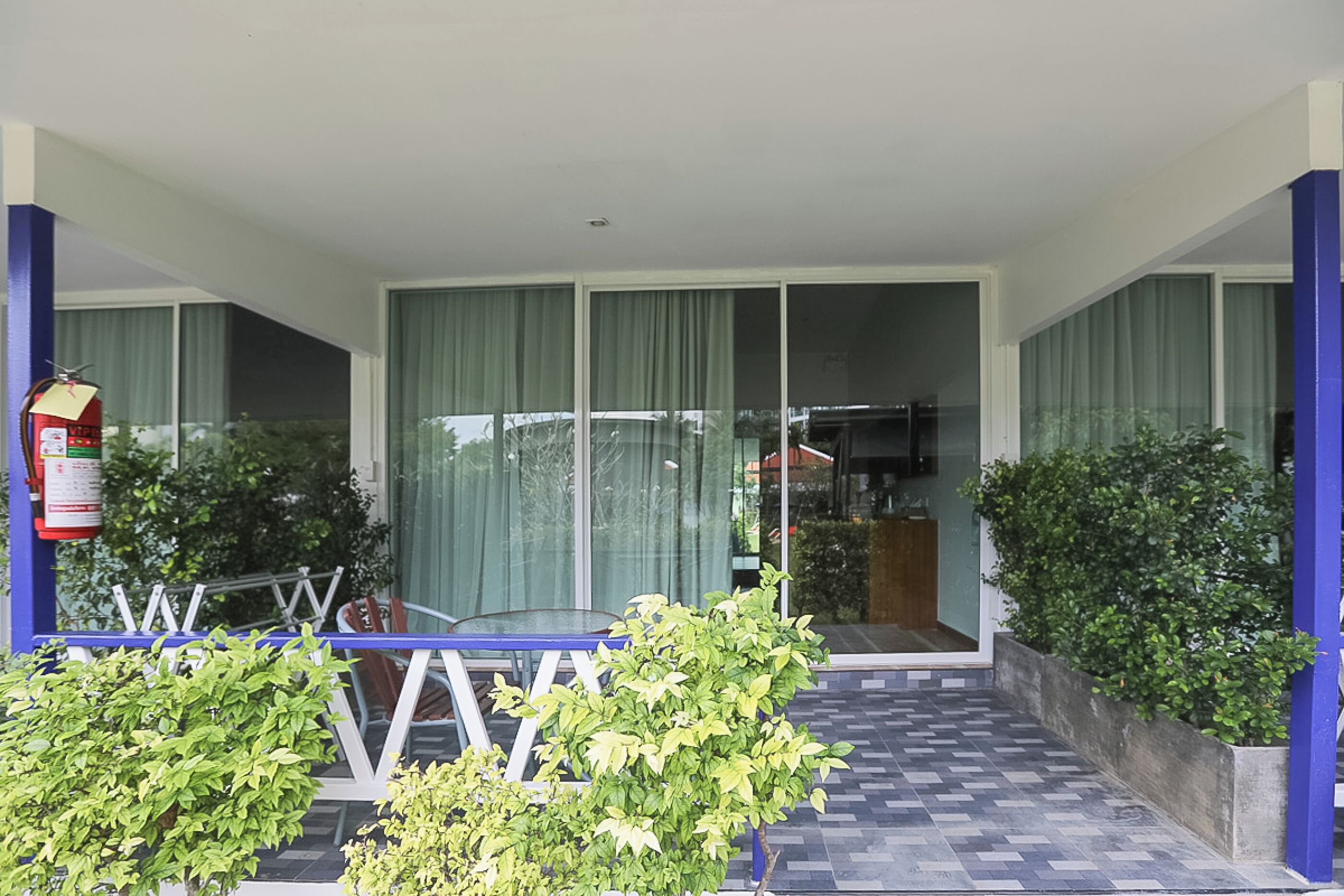 A hotel entrance with a glass door, a fire extinguisher on the left, and a blue railing in the foreground.