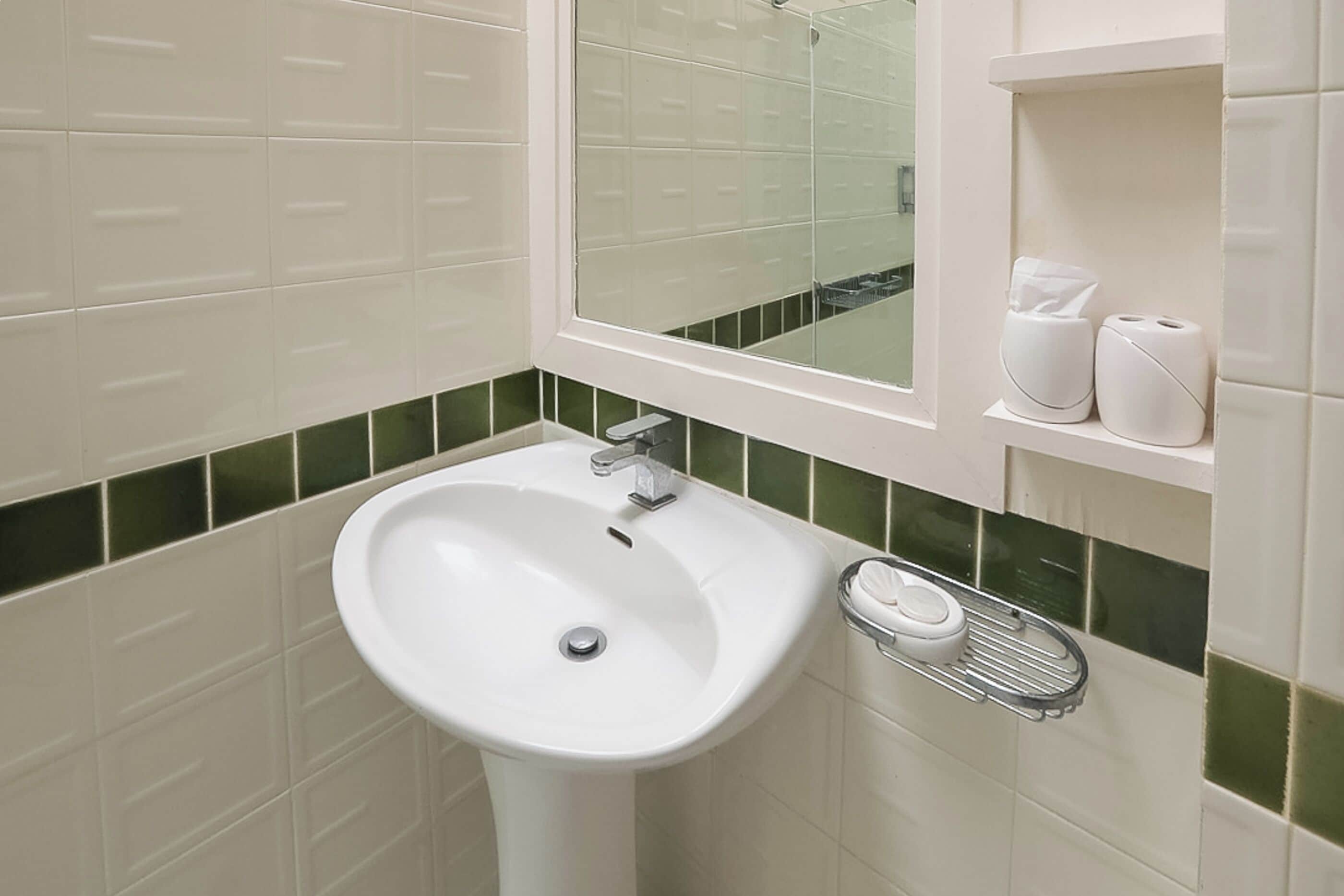 A bathroom with a white pedestal sink, a mirror above it, and a shelf with toiletries.