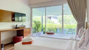 Habitación de hotel con dos camas, un escritorio de madera, televisión y balcón con vistas a zonas verdes.
