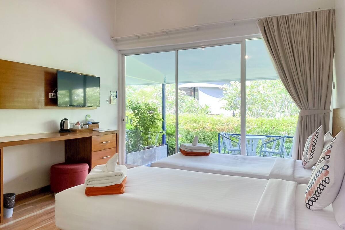 Une chambre d’hôtel avec deux lits, un bureau en bois, une télévision et un balcon donnant sur un paysage verdoyant.
