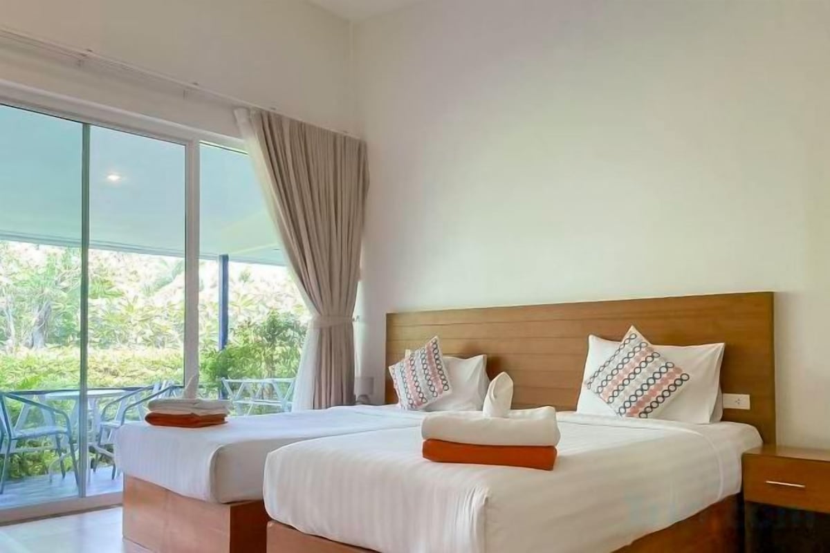 A hotel room with two beds, a balcony, and a view of greenery.