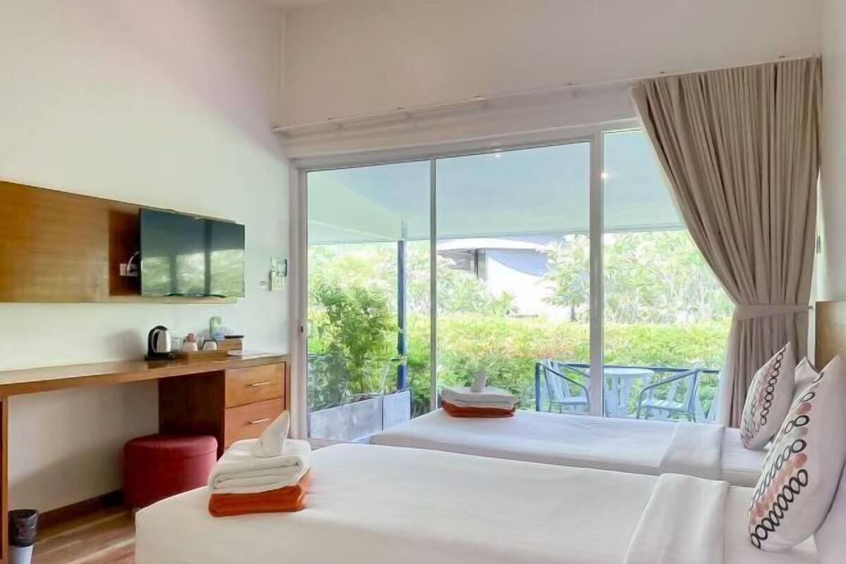 Une chambre d’hôtel avec deux lits, un bureau, une chaise et une grande fenêtre donnant sur un paysage verdoyant.
