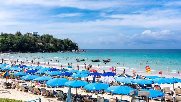 Una playa con muchas sombrillas azules, sillas de playa y gente nadando.