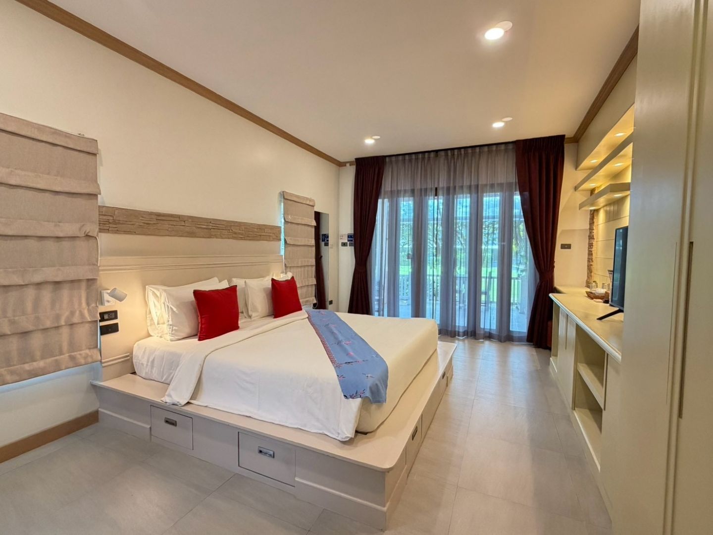 A hotel room with a large bed, bedside tables, a TV, and a view of the outdoors.